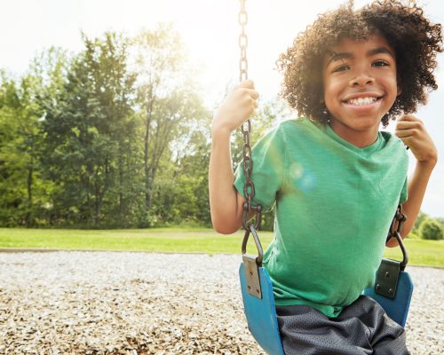 African boy, portrait and smile with park, swing and nature for outdoor fun and play with fresh air. Child, tree and playground with summer, freedom and school holiday or break outside with happiness.
